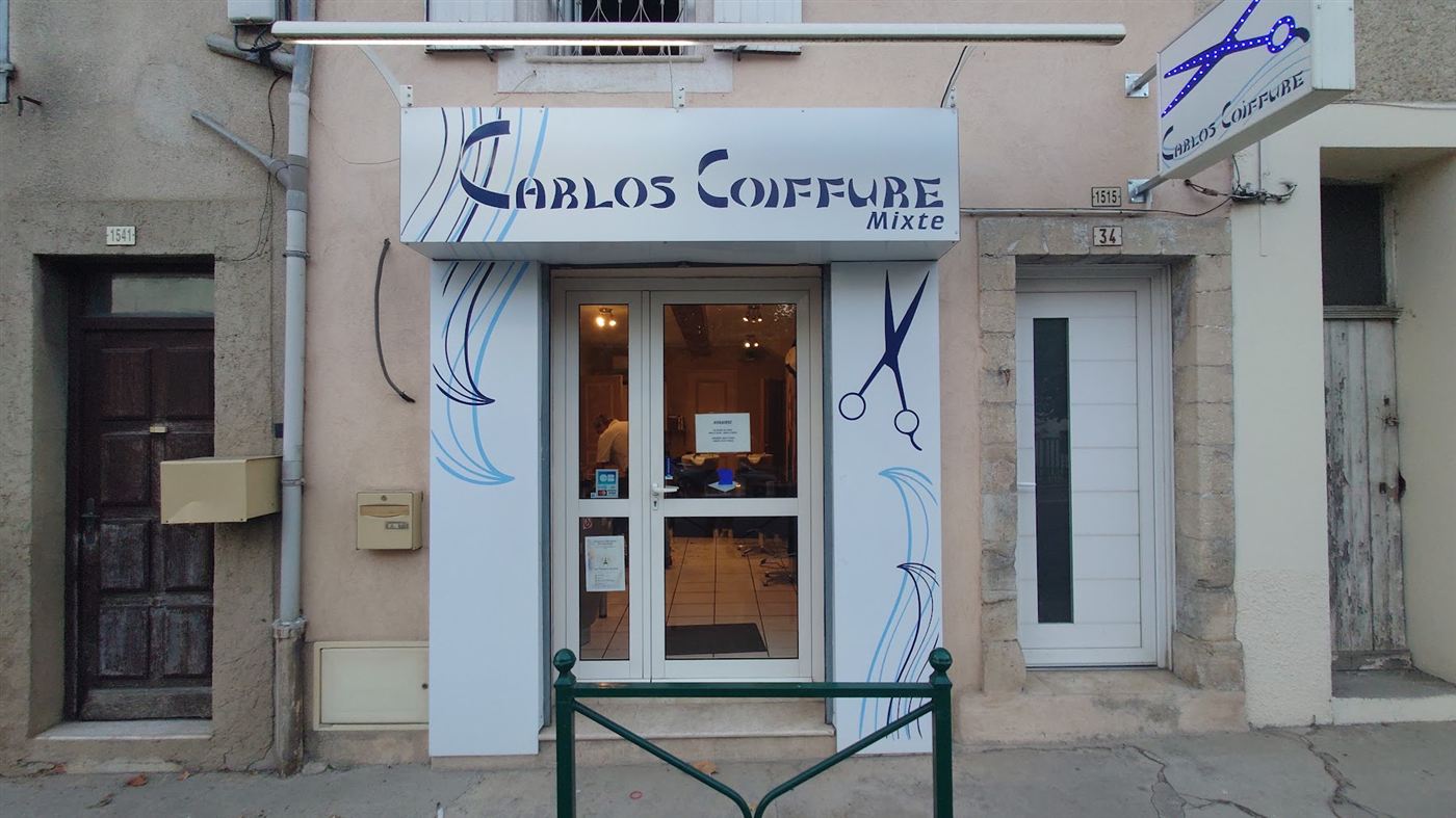 Façade de jour du salon Carlos Coiffure, enseigne bleue et ciseaux dessinés sur les panneaux