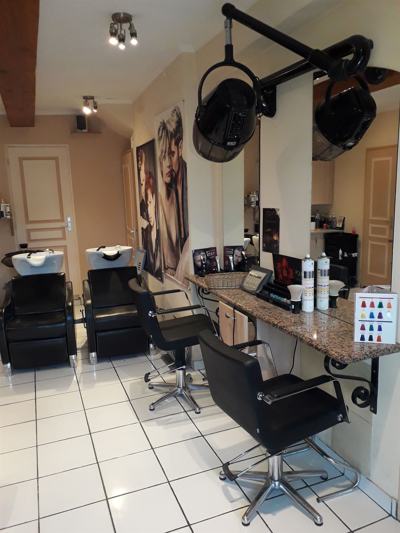 L’intérieur du salon : bacs à shampooing, fauteuils noirs et casque sèche-cheveux