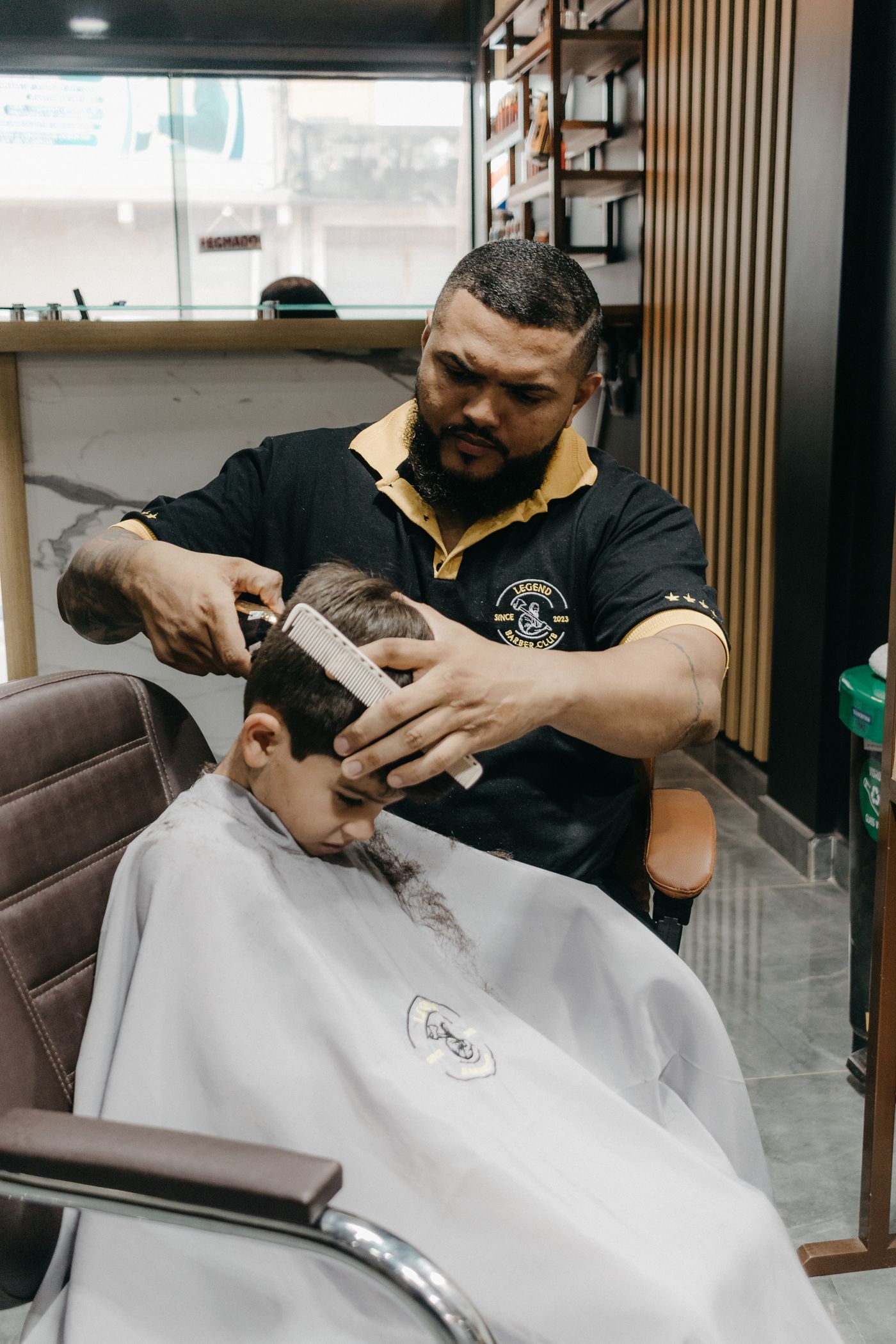 Un petit garçon coiffé par un coiffeur concentré, dans un salon lumineux