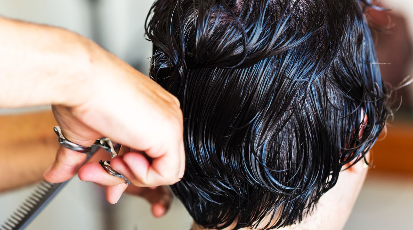 Ciseaux coupant des cheveux courts et sombres encore mouillés