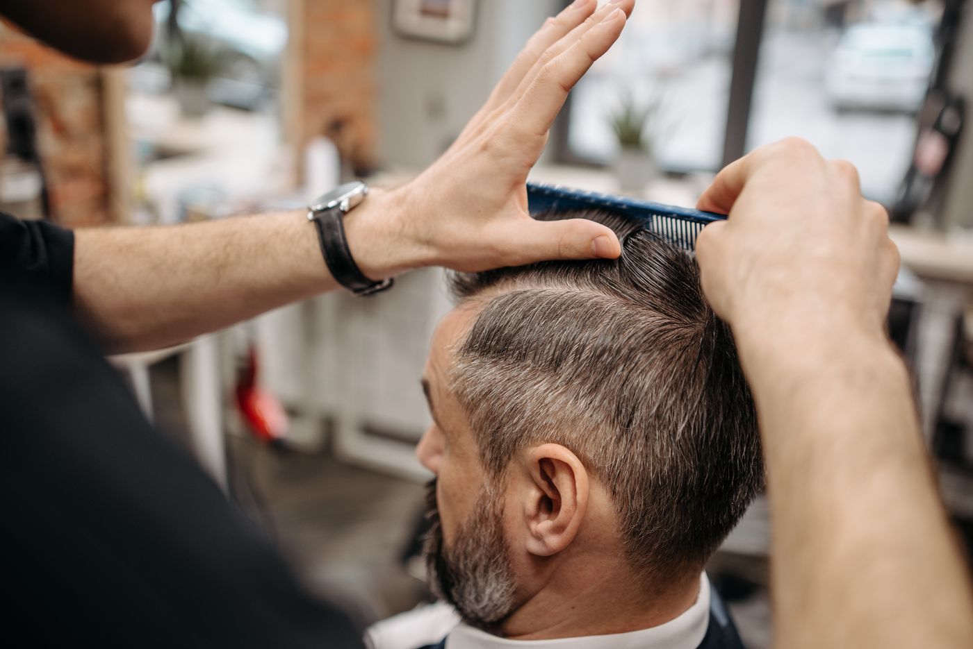 Mains d’un coiffeur au peigne et au ciseau sur la coupe d’un client